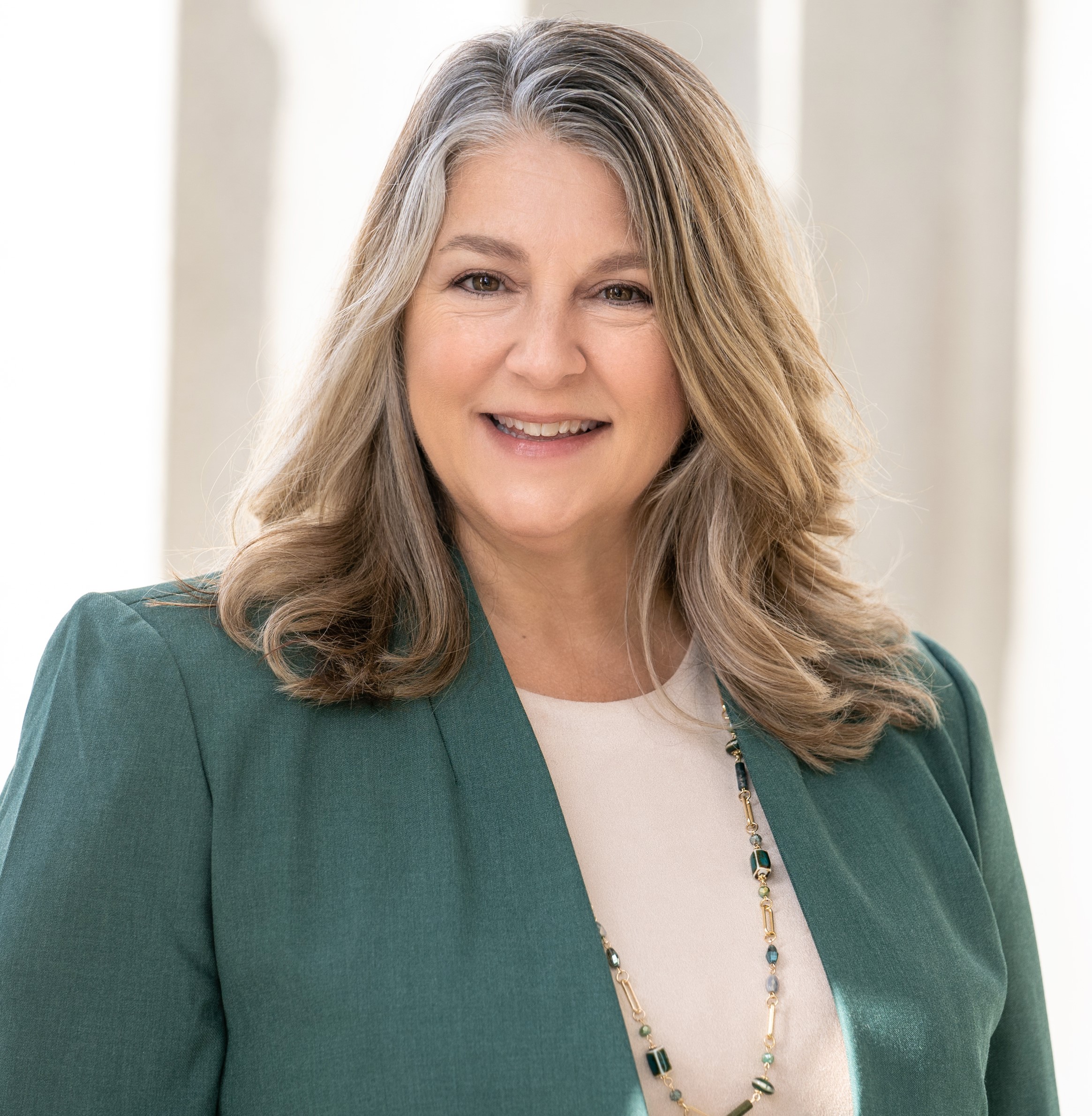 Shoulder-length blonde-haired woman in green blazer and white blouse