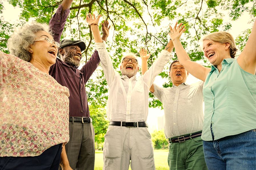 group of older adults in a circle with arms raised outdoors under a tree
